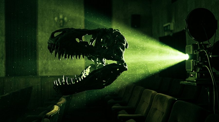 Siluet kepala tyrannosaurus rex menganga di depan layar proyektor sinematik dengan cahaya hijau dramatis